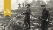 Zwei Helfer in Uniform halten einen Schlauch beim Löschen von Moorbrand  