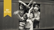 Fünf Kinder winken zum Abschied aus dem Fenster eines abfahrenden Zugwaggons (1959)  