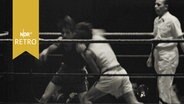 Zwei Boxer beim Kampf im Ring, daneben der Schiedsrichter  