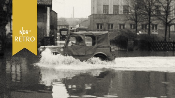 Militärjeep bei Fahrt durch eine überschwemmte Stadtstraße (1962)  