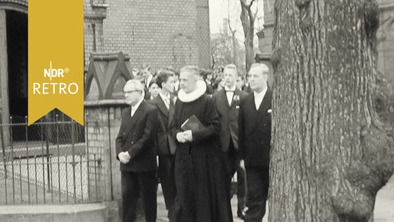 Pastor führt Zug der Konfirmanden vor der St. Johannis-Kirche in Harvestehude an (1960)  