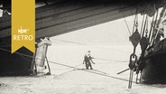 Zwei Arbeiter auf einem Schiffsrumpf im Wasser zwischen zwei Bergungsschiffen  