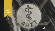 Arzt-Schild mit Äskulapstab hinter einer Glasscheibe (1960)  