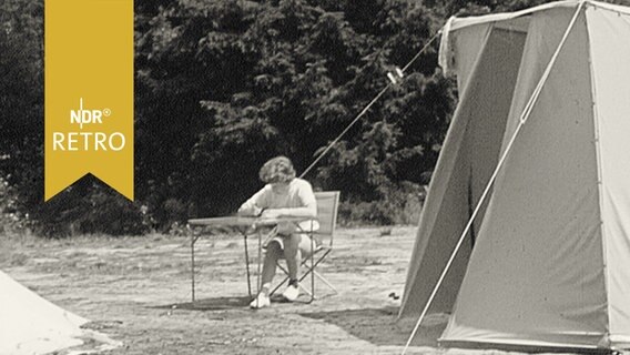 Frau liest ein Buch am Campingtisch neben einem Zelt (1960)  