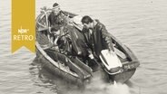 Drei Skipper in einem Motorboot blicken ins Wasser (1960)  