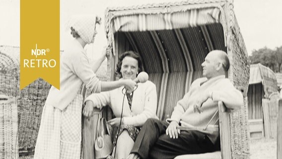 Ein Ehepaar wird, in einem Strandkorb sitzend, von einer Reporterin befragt.  