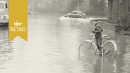 Überschwemmte Straße in Bad Bentheim mit einem stehenden Radfahrer und einem fahrenden VWQ Käfer (1960)  