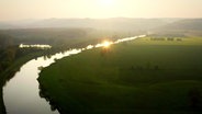 Die Weser umringt von grünen Feldern und Wäldern im Sonnenuntergang.  