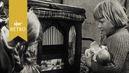 Mädchen mit Puppe im Arm steht fasziniert vor einer Drehorgel (1955)  