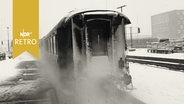 Ein Personenzug fährt in einen winterlichen Bahnhof ein (1960)  