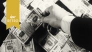 Eine Hand greift sich aus einem Haufen gebündelter DM-Scheine ein Bündel mit 10-Markscheinen heraus (1963)  