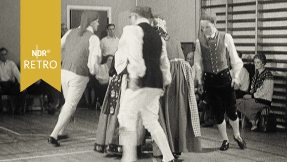 Kostümierte Menschen in Trachten beim Üben eines Volkstanzes in einer Turnhalle (1964)  