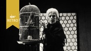 Bild aus einer Inszenierung des Stückes "Hochzeit" von Elias Canetti. Eine alte Frau mit einem Vogelkäfig (1965)  