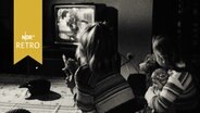 Zwei Mädchen am Wohnzimmertisch vor einem Fernsehgerät (1964)  