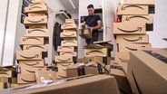 Ein junger Mann sitzt inmitten von Amazon-Paketen.  