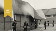Feuerwehrleute demonstrieren 1961 das Löschen eines brennenden Reetdaches  