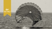 Marinetaucher krault im Meer, während hinter ihm sein Fallschirm im Wasser landet  