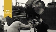 Mitarbeiter einer Filmcrew postieren Scheinwerfer vor einem Schiff im Lübecker Hafen (1961)  