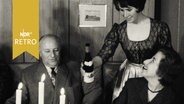 Kellnerin schenkt älterem Paar an einem Tisch Wein ein (1961)  