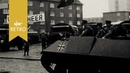Bundeswehrfahrzeuge und ein Schützenpanzer mit Besatzung auf einem Platz, mit NATO-Flagge und Transparent "Unser Heer" (Ausstellung der Bundeswehr 1961)  