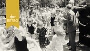 Kinder rennen durch ein Tor auf das Gelände des neu eröffneten Feriendorfs Neumünster (1961)  