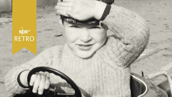 Kind in einem Modellauto grüßt in die Kamera (1965)  