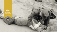 Ersthelfer des DRK bei einer Übung, legen einem Opfer einen Bein-Verband an (1961)  
