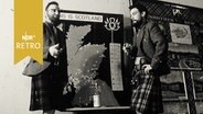 Zwei Männer im schottischen Kilt garnieren ein Ausstellungsplakat "This is Scotland" in Hamburg 1961  