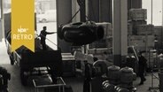 Maschinenteile werden in einer Halle auf einen LKW geladen (1961)  