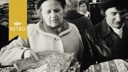 Zwei ältere Kundinnen begutachten Hemden an einem Grabbeltisch (1962)  