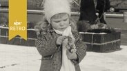 Kind in winterlicher Kleidung zupft an einem kleinen Blumenstrauß zum Valentinstag1962  