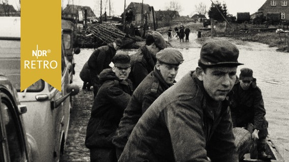 Mehrere Männer ziehen an einem Tau, um ein havariertes Boot - nicht im Bild - frei zu bekommen (Sturmflutkatastrophe 1962)  