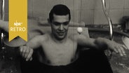 Junger Mann demonstriert ein Moorbad in einer Wanne auf Heilmittelausstellung in Pyrmont 1962  