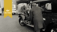 Männer schieben ein geschmücktes Taxi (Hannover 1962).  