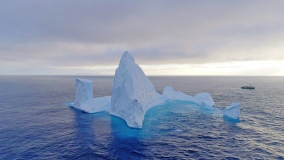 Im Südpolar-Meer treibender Eisberg; aus der Luft aufgenommen. Ganz klein im Hintergrund ein Schiff von Greenpeace. © NDR/HTTV 
