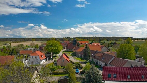 Blick auf ein Dorf im Frühling von einem erhöhten Standpunkt aus: Häuser, grüne Bäume und blauer Himmel. © MDR/Hoferichter & Jacobs 
