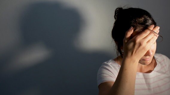 Eine Frau, die in der rechten unteren Ecke des Bildes platziert ist, hält sich den Kopf. Ihr Gesicht ist kaum zu erkennen. An der Wand hinter ihr sieht man ihren Schatten. © picture alliance / dpa | Oliver Killig Foto: Oliver Killig