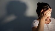 Eine Frau, die in der rechten unteren Ecke des Bildes platziert ist, hält sich den Kopf. Ihr Gesicht ist kaum zu erkennen. An der Wand hinter ihr sieht man ihren Schatten. © picture alliance / dpa | Oliver Killig Foto: Oliver Killig