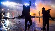 Ausschreitungen am 07.07.2017 in Hamburg. Nachtszene. Drei oder vier schwarze Gestalten von hinten aufgenommen, werfen mit Steinen oder Flaschen. Die Straße ist nass vom Wasserwerfereinsatz. Im Hintergrund brennt ein Feuer. © picture alliance / R. Goldmann 