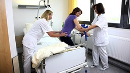 Zwei Krankenschwestern stützen eine Patientin auf Krücken Zwei Krankenschwestern stützen eine Patientin auf Krücken © imago/Jochen Tack