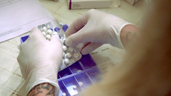 Hände mit Handschuhen drücken Tabletten aus einem Blister heraus. © NDR 