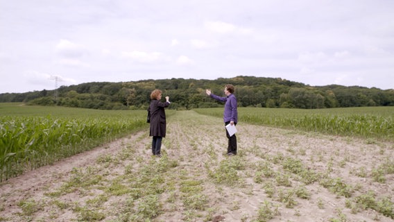 Autor Malte Heynen steht mit seiner Kollegin Gesine Enwaldt auf einen Streifen Ackerland und zeigt den Verlauf der Gaspipeline, die dort gebaut werden soll. © NDR/Filme & Consorten Produktionsgesellschaft 