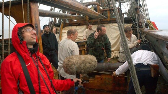 Regisseur Florian Dedio bei den Dreharbeiten auf einer historischen Fregatte. Es regnet - genau wie vor 300 Jahren, als die Seeschlacht vor Rügen tatsächlich stattfand. © NDR/Marcel Wollgast 