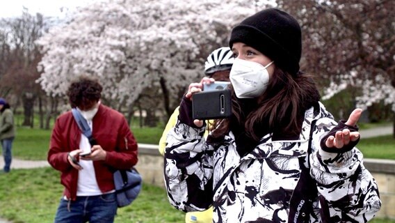 Lokalreporterin Franziska Klemenz mit Maske hält ihr Handy vor sich und filmt. © NDR/Laura Borchardt 