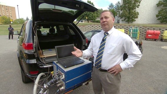 Dan Carder von der West Viriginia University, am Heck eines Autos, an das ein Abgasprüfgerät angeschlossen ist. © NDR 