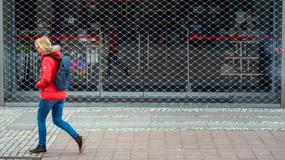 Eine Frau geht an einem mit einem Gitter verschlossenen Geschäft vorbei. © picture alliance/Gregor Fischer/dpa Foto: Gregor Fischer