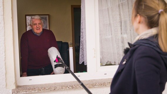 Eine junge Frau hält ein langes Mikrofon in ein Fenster. Ein älterer Mann spricht hinein. © NDR/7 Tage 