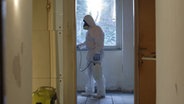 Ein Mann in weißem Schutzanzug und Maske reinigt eine Wohnung. © NDR/7Tage 