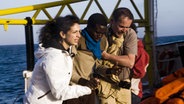 Zwei Menschen helfen einem Flüchtling aufs Schiff. © NDR 