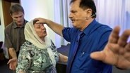 Pastor Seifert legt einer Frau die Hand auf den Kopf. © NDR 